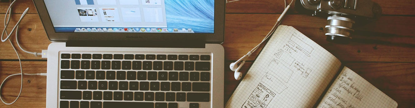 Wooden cafe tabletop with a computer, journal, and camera