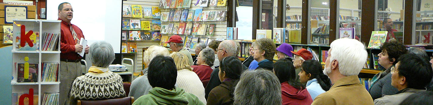 Community members sitting in rows of chairs at the library, listening to a speaker