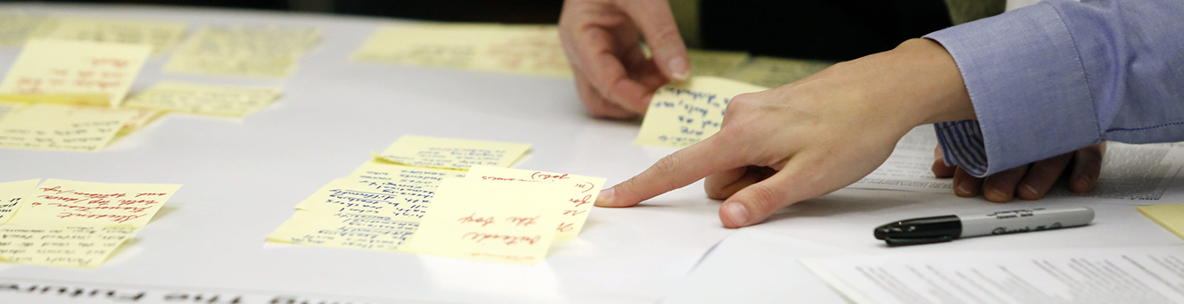 A sticky note organizational chart, being assembled by two people whose hands are shown
